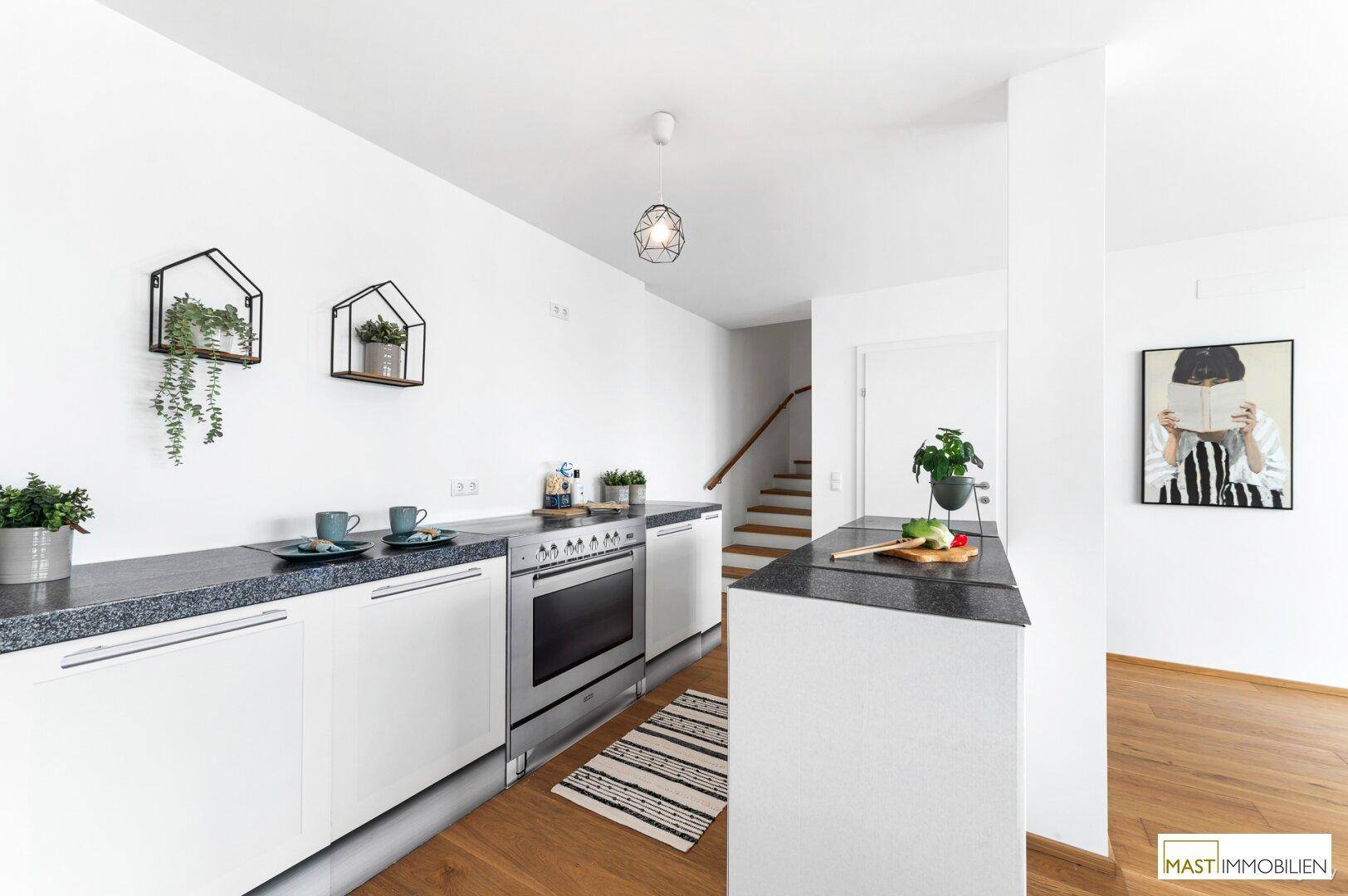 Moderne Küche mit weißen Schränken, dunkler Arbeitsplatte und integriertem Backofen.