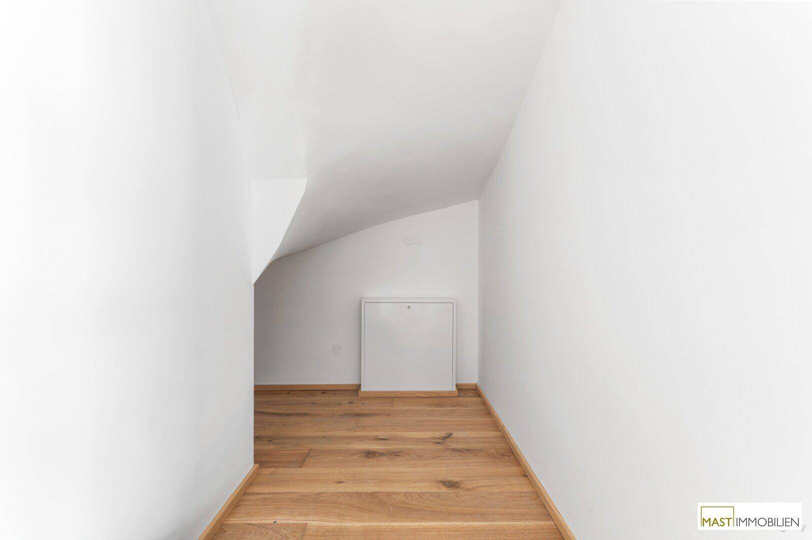 Schmaler Raum im Dachgeschoss mit Holzboden und schrägen Wänden, ideal als Abstellraum.