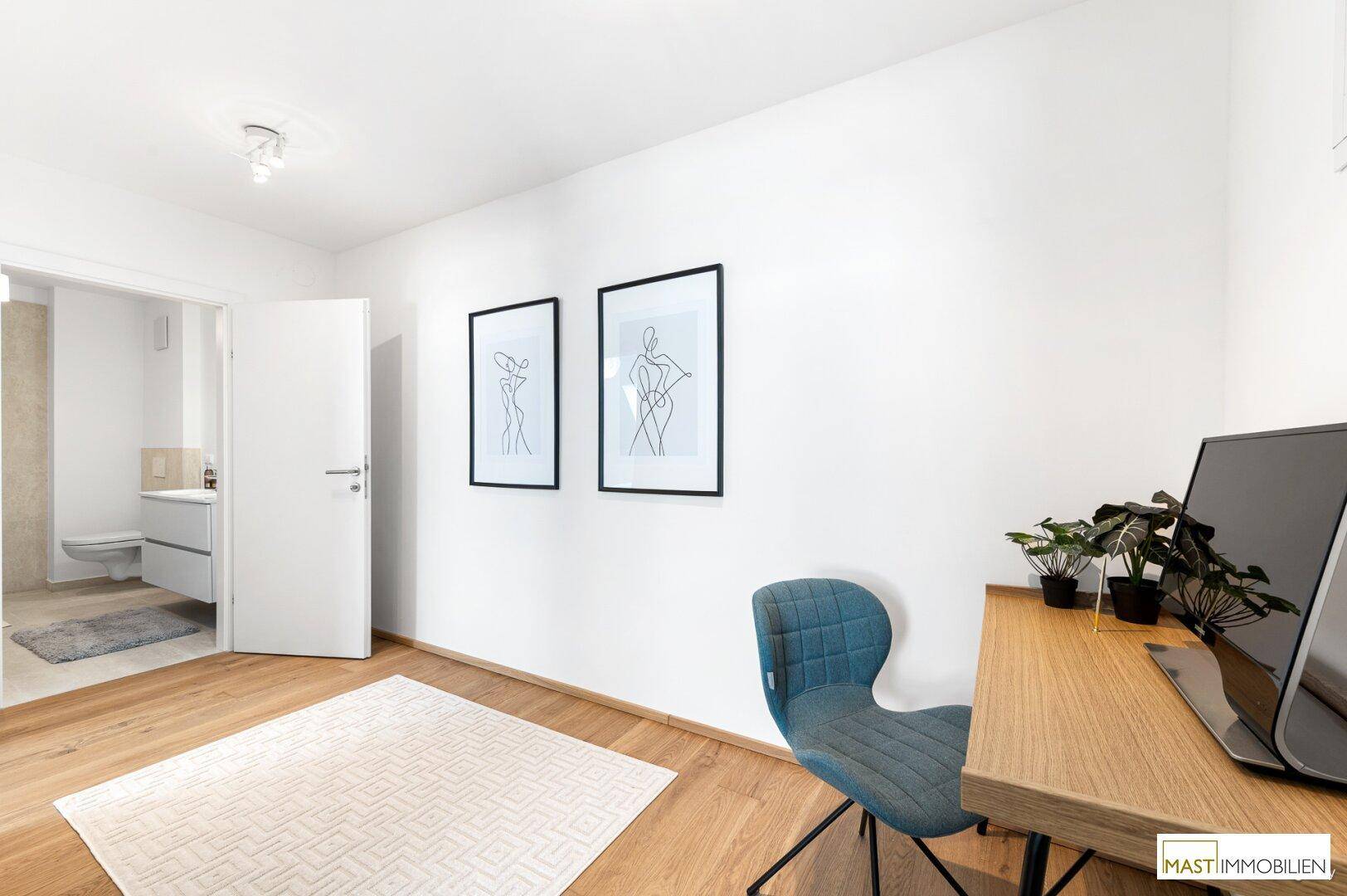 Helles Arbeitszimmer mit Holzboden, Schreibtisch und Zugang zu einem angrenzenden Badezimmer.