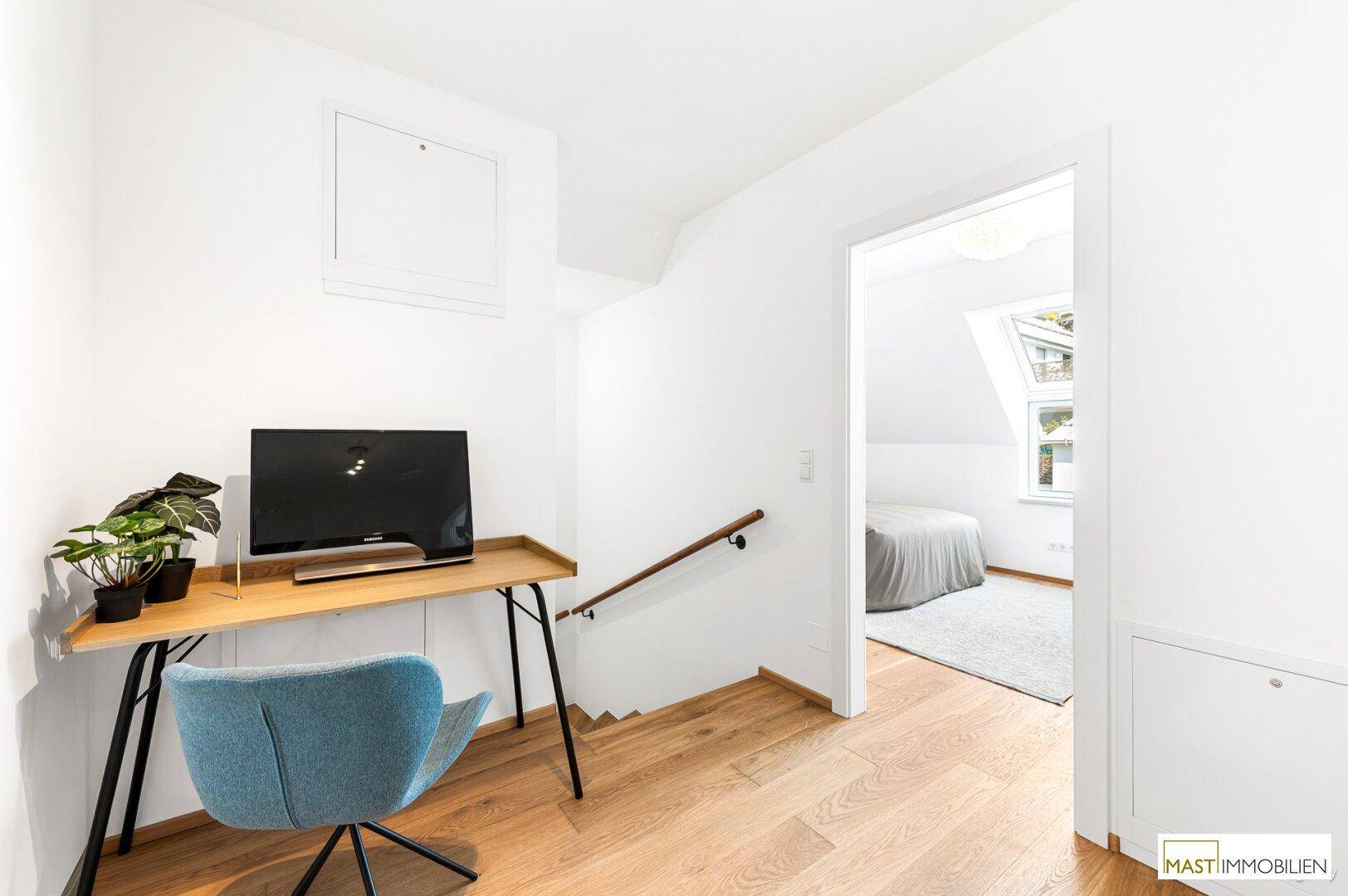 Heller Flur mit kleinem Arbeitsbereich und Blick in ein Schlafzimmer im Dachgeschoss.