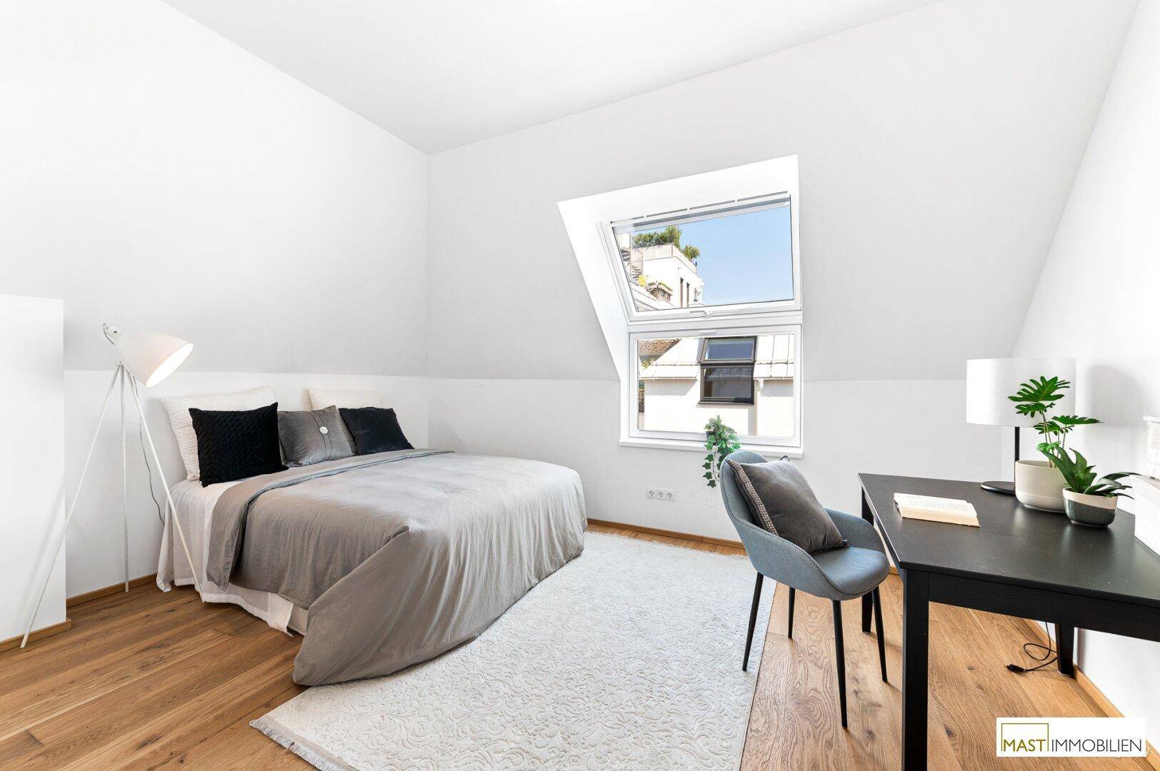 Gemütliches Schlafzimmer im Dachgeschoss mit Bett, Schreibtisch und großem Dachfenster.