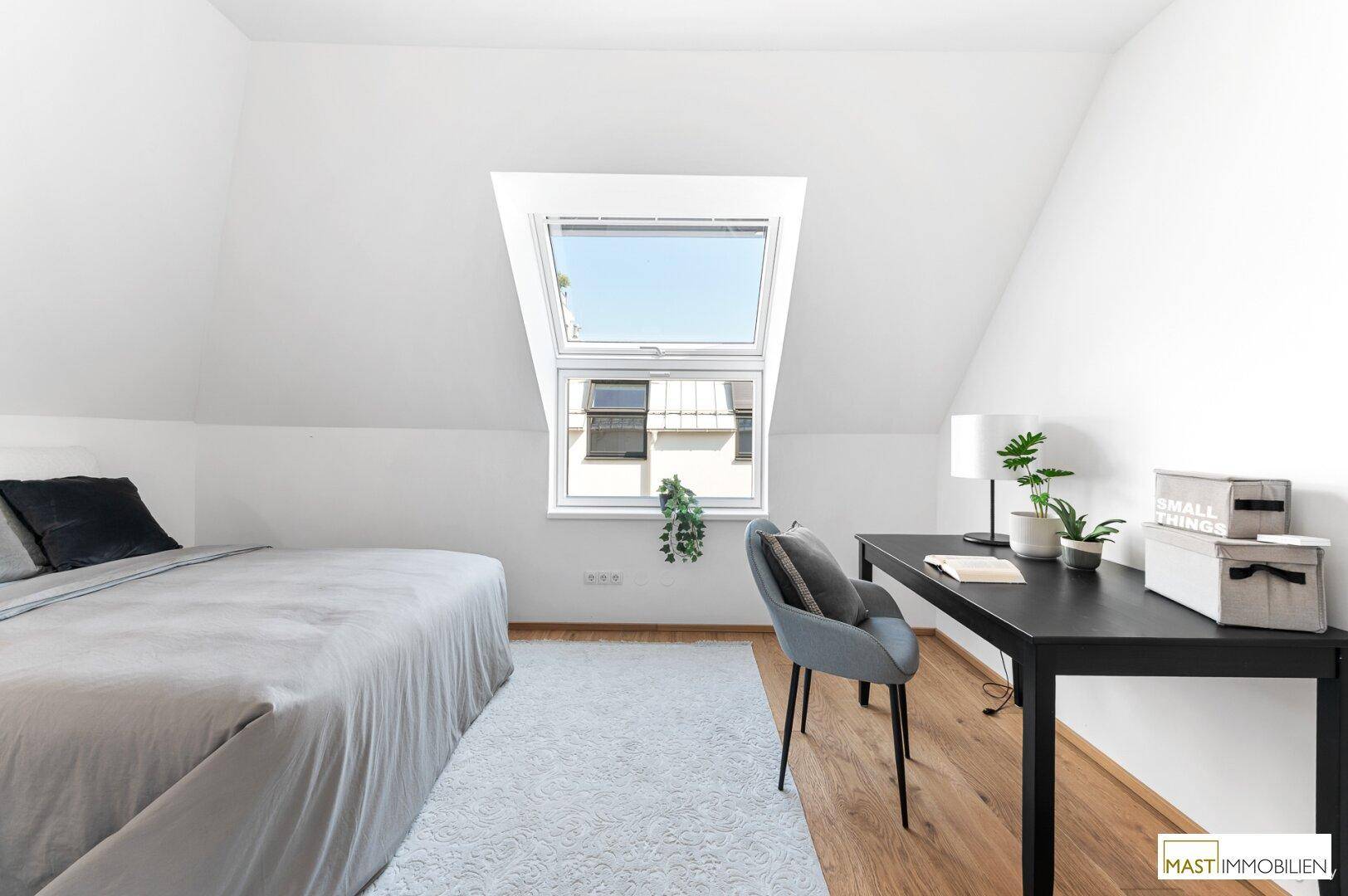 Helles Schlafzimmer im Dachgeschoss mit Bett, Schreibtisch und viel Tageslicht durch das Dachfenster.