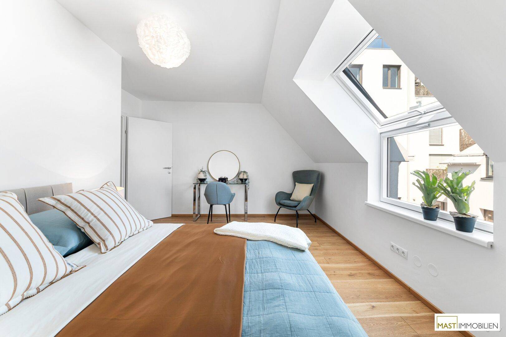Helles Schlafzimmer im Dachgeschoss mit Holzboden, großem Bett und einem Schminktisch unter dem Dachfenster.