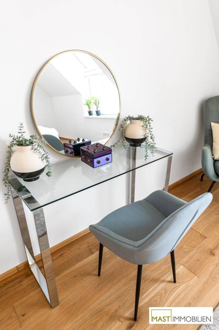 Detailansicht eines modernen Schminktisches mit Glasplatte und rundem Spiegel in einem Schlafzimmer.