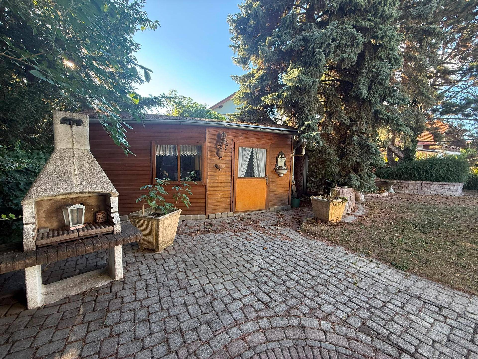 Gartenbereich mit Holzschuppen, gemauertem Grill und gepflastertem Sitzplatz.
