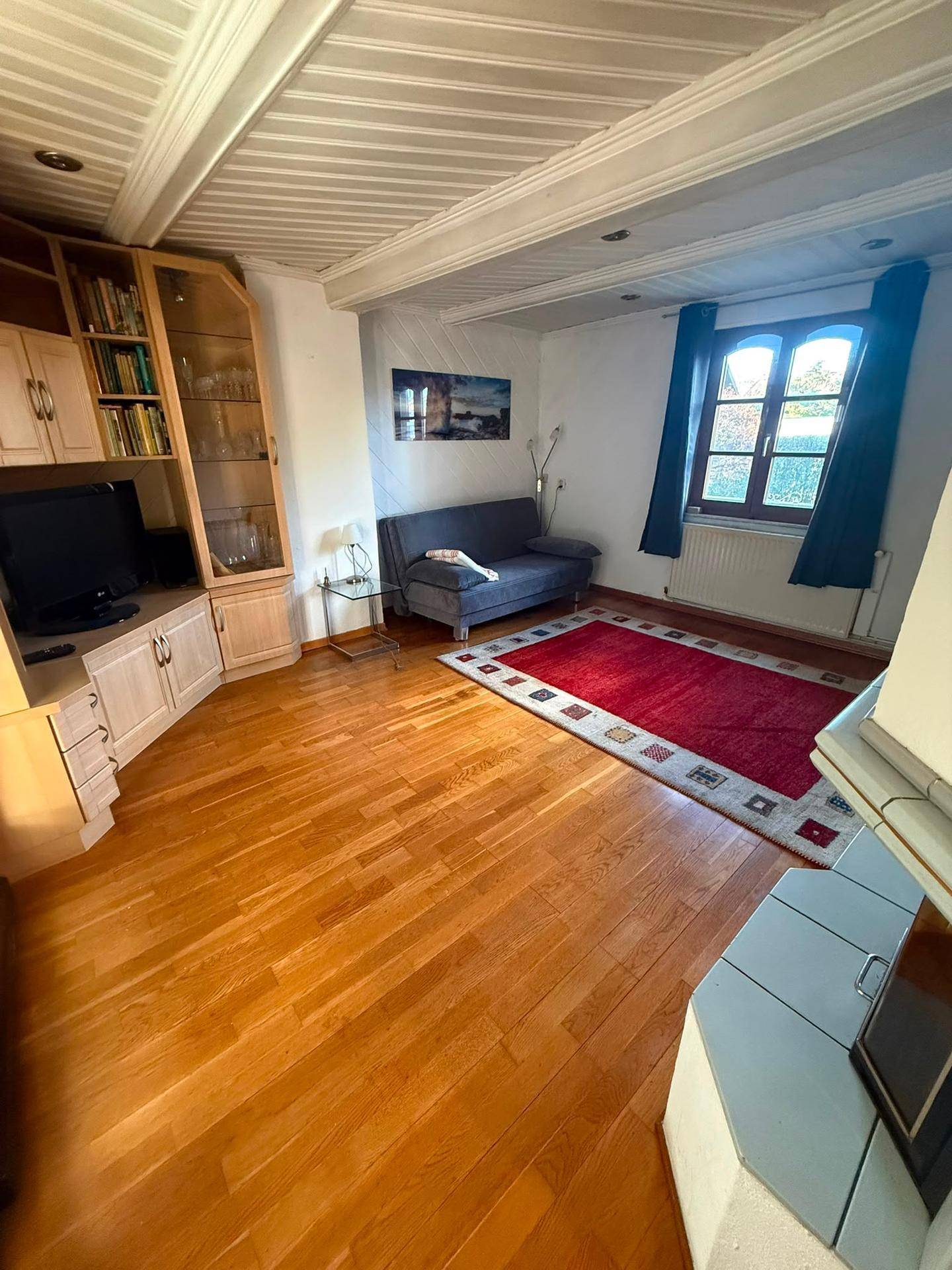 Gemütliches Wohnzimmer mit Holzboden, Kachelofen und Blick nach draußen.