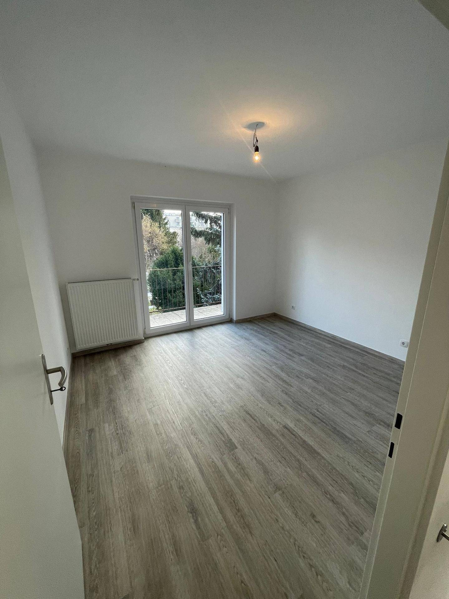Helles Zimmer mit Laminatboden und einer französischen Balkontür, die viel Licht hereinlässt.