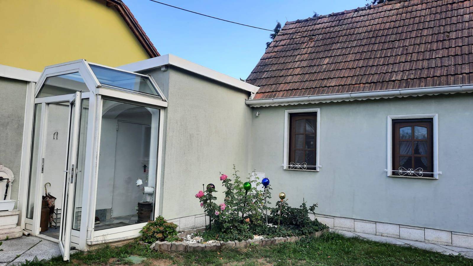 Hausfassade mit kleinem Vorgarten, Rosenbüschen und einem verglasten Eingangsbereich.