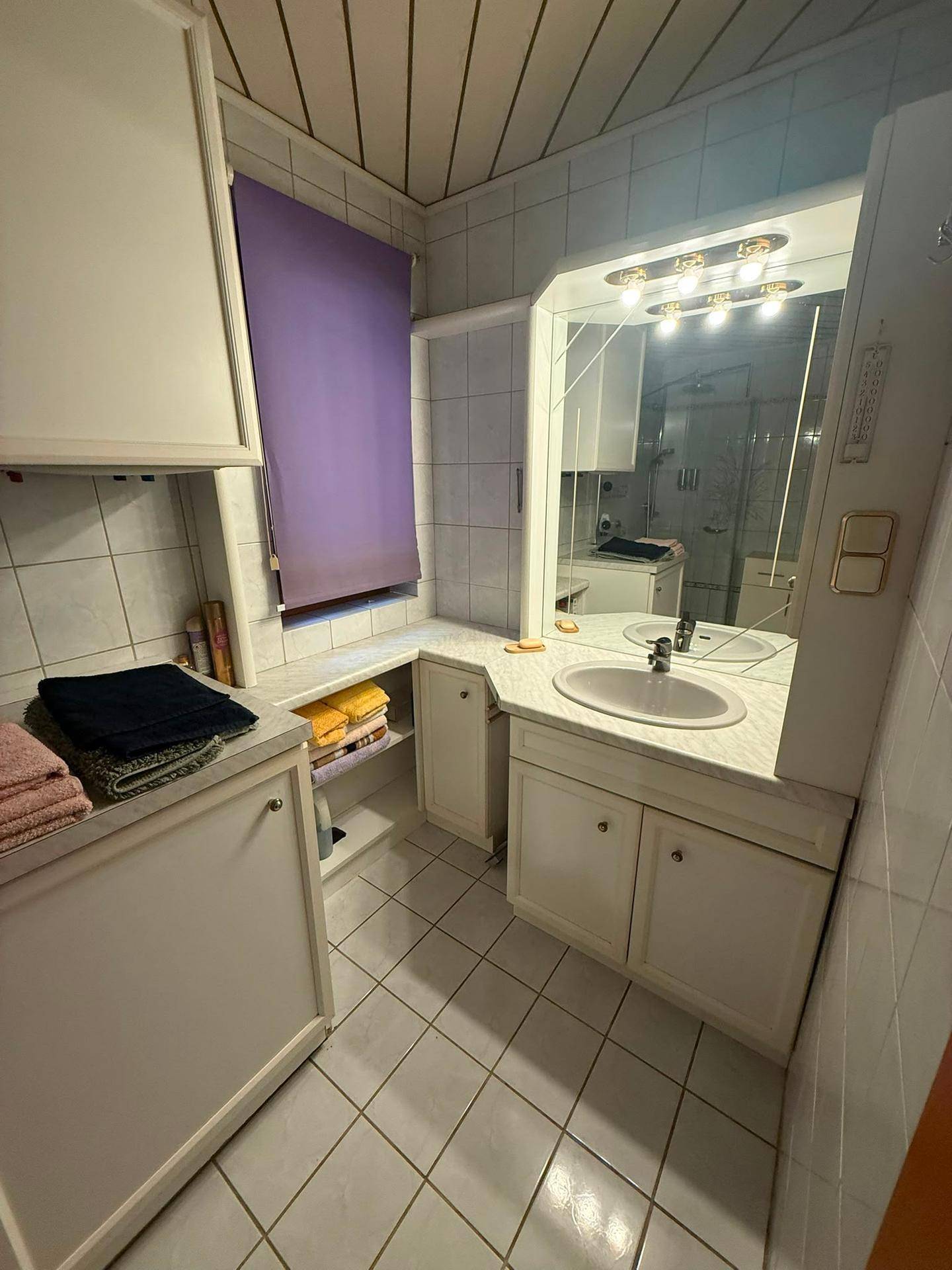 Badezimmer mit weißem Waschtisch, Spiegelschrank und hellen Fliesen.