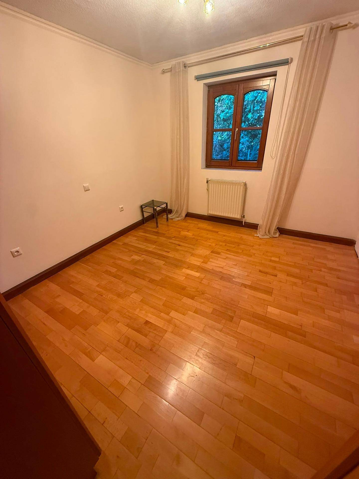 Leeres Schlafzimmer mit Holzboden, Fenster und Heizkörper.