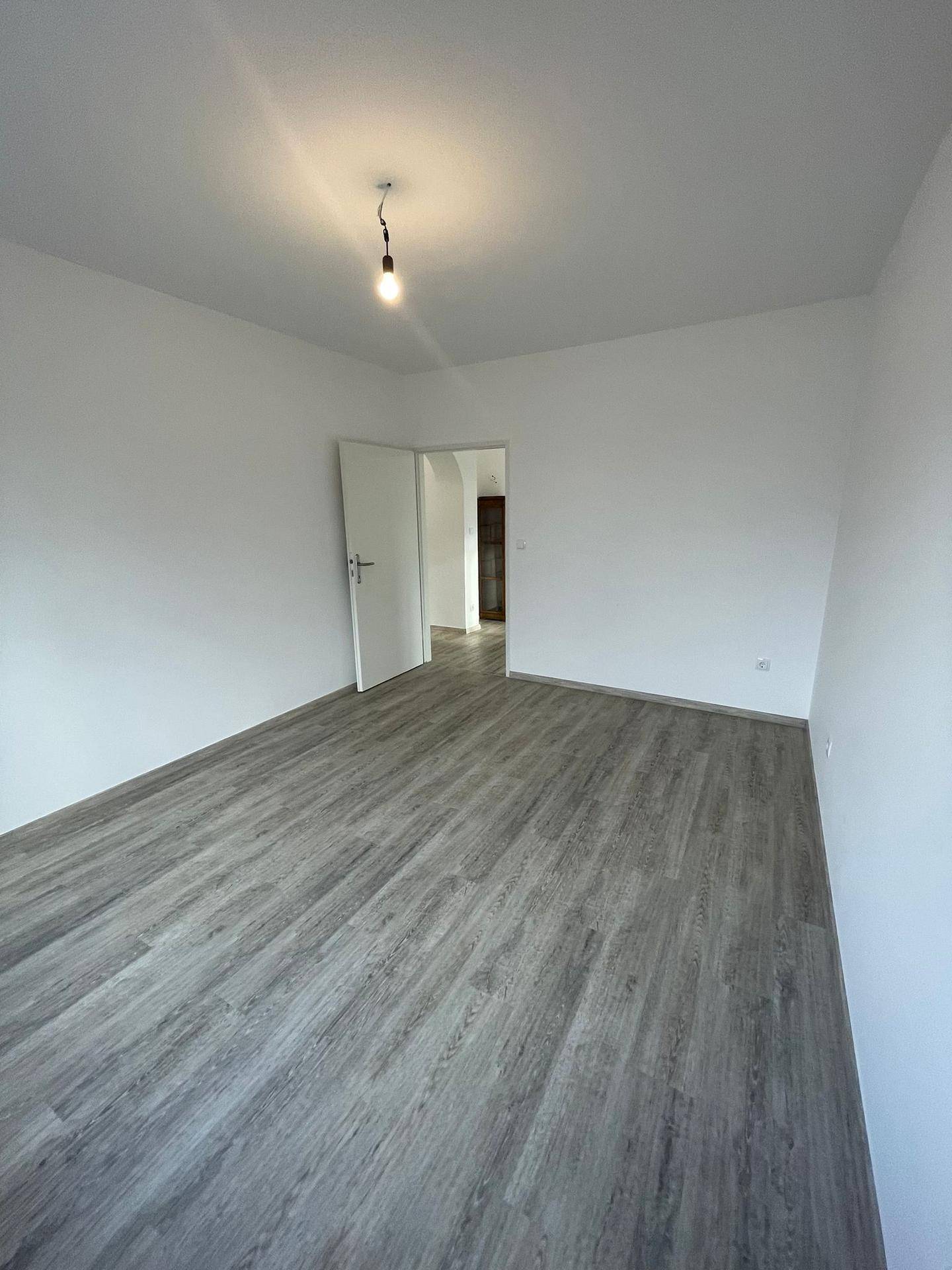 Geräumiges, leeres Zimmer mit hellem Laminatboden und weiß gestrichenen Wänden.