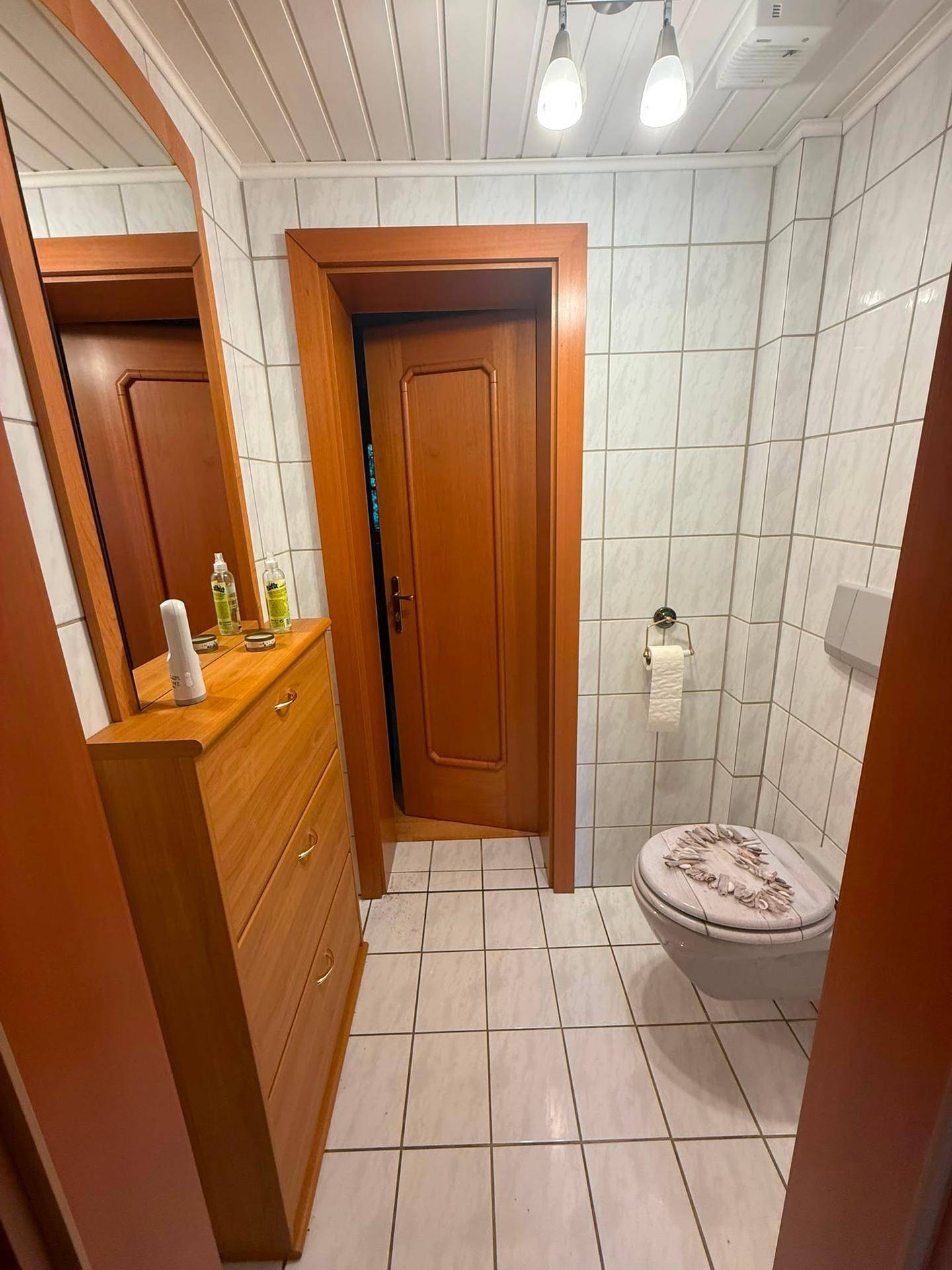Gäste-WC mit Wand-WC, hellen Fliesen und Holzdetails.