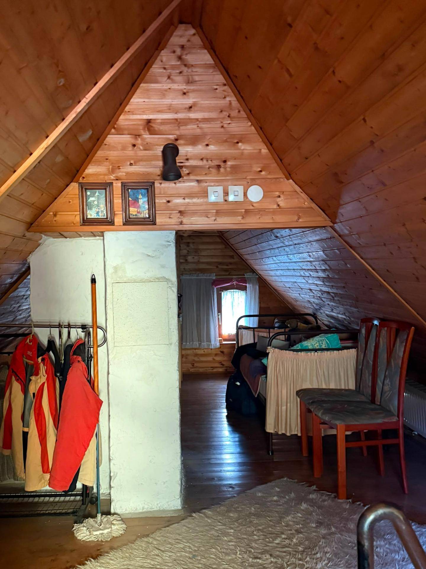 Dachgeschosszimmer mit Holzverkleidung, schrägen Wänden und einfacher Einrichtung.