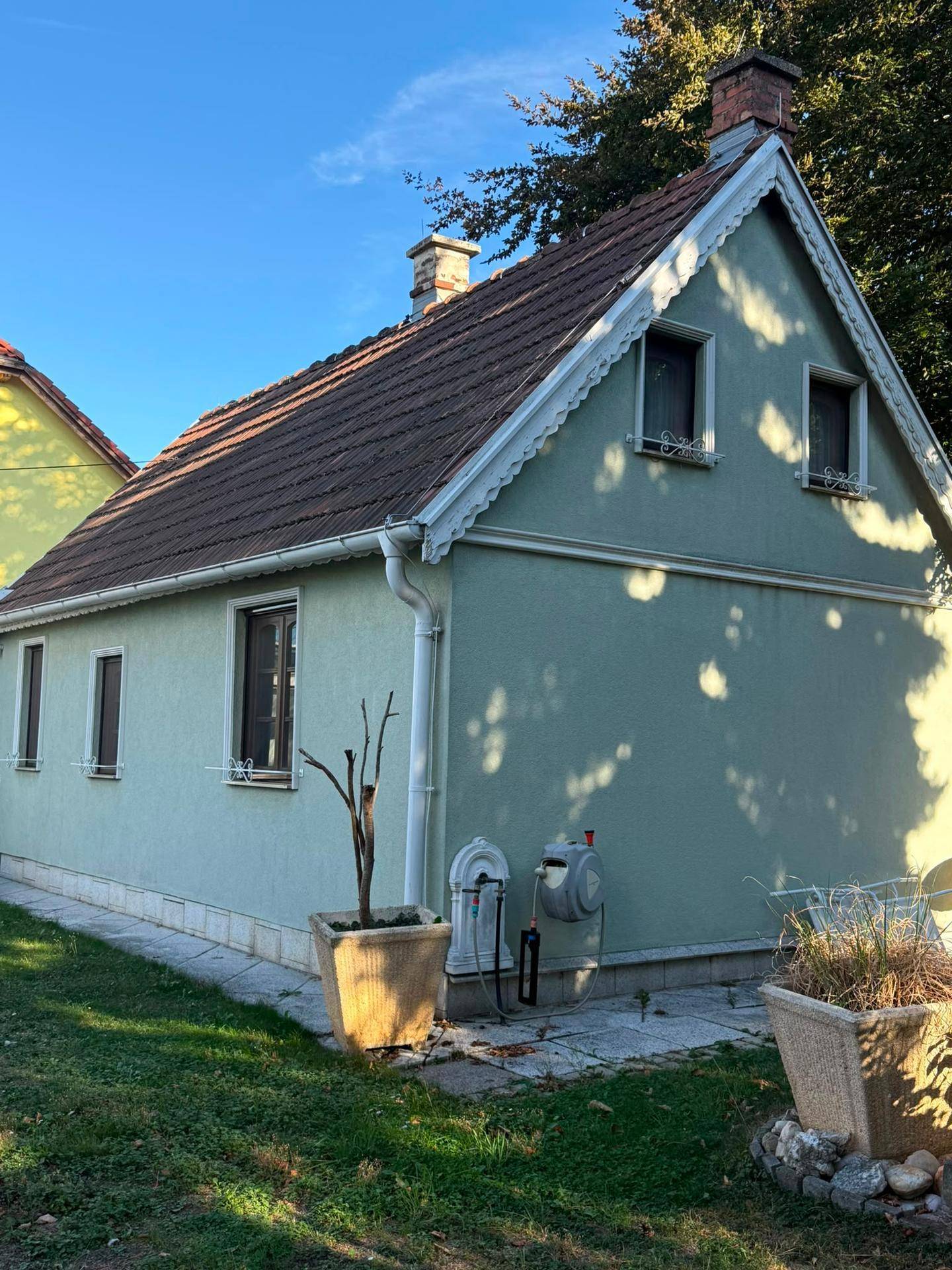 Seitenansicht des Hauses mit grüner Fassade, Satteldach und kleinen Fenstern.