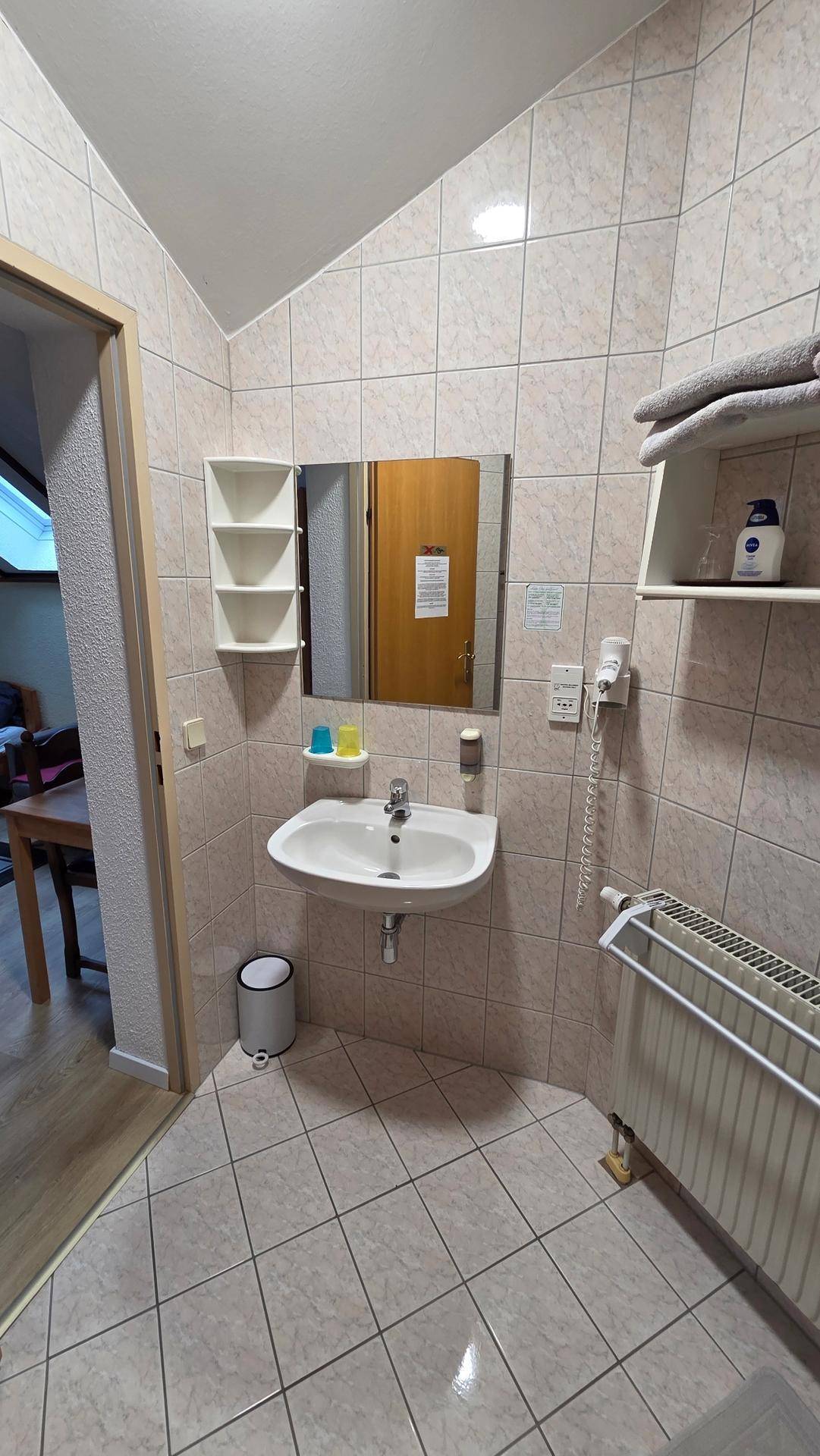 Badezimmer mit beigefarbenen Fliesen, Waschbecken mit Spiegel und Handtuchheizkörper.
