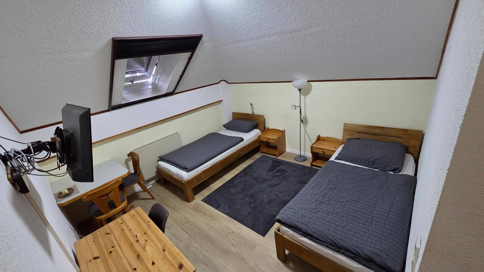 Dachgeschosszimmer mit zwei Einzelbetten, Esstisch, Wandfernseher und einem Dachfenster.