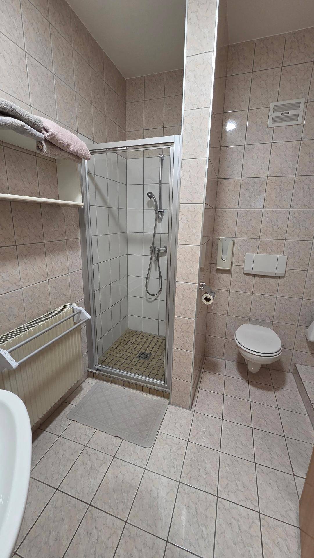 Badezimmer mit beigefarbenen Fliesen, Duschkabine und wandhängendem WC.