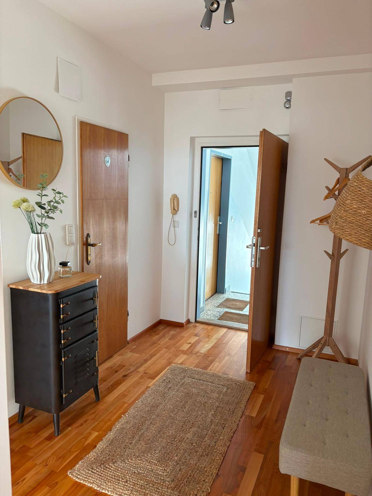 Eingangsbereich mit Holzboden, Spiegel und Garderobe, der zur Wohnungstür führt.
