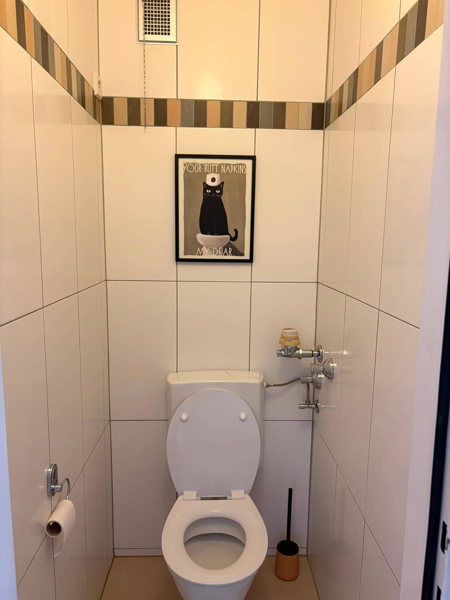Separates WC mit Toilette und weißen Fliesen, dekoriert mit einem Bild.
