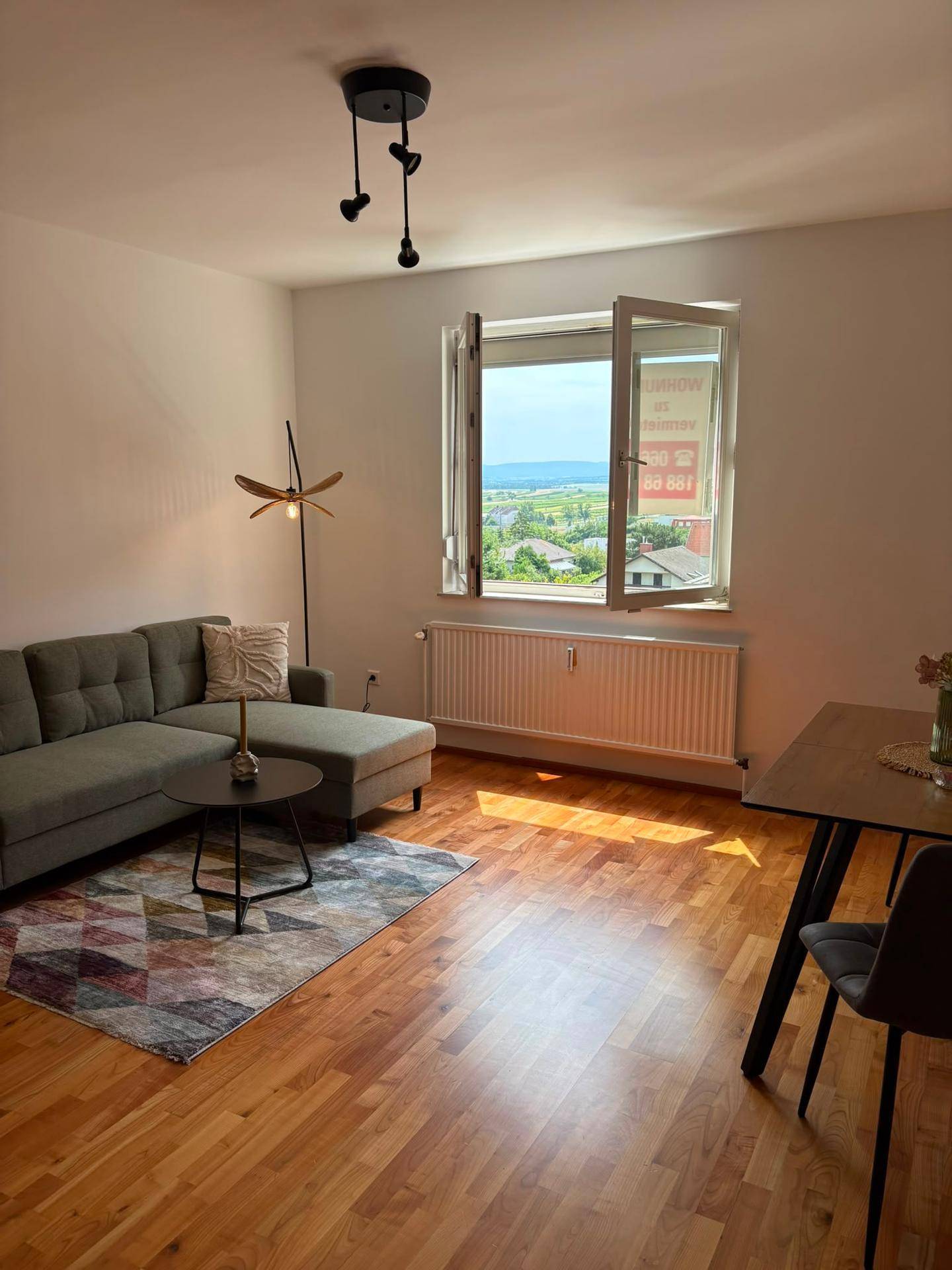 Heller Wohnbereich mit bequemer Couch, Holzboden und weitem Blick aus dem Fenster.