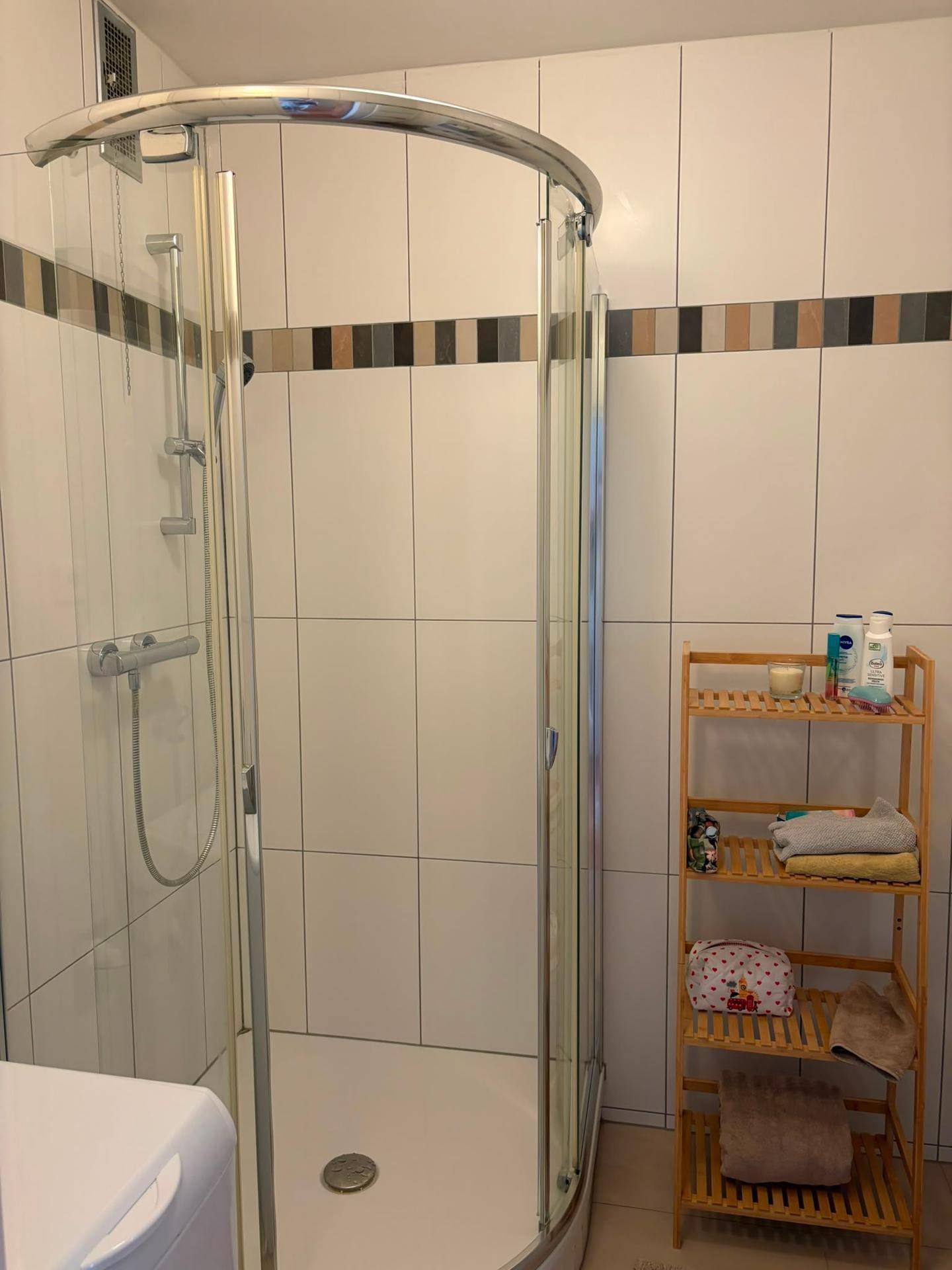 Badezimmer mit Duschkabine, weißen Fliesen und einem Holzregal für Utensilien.