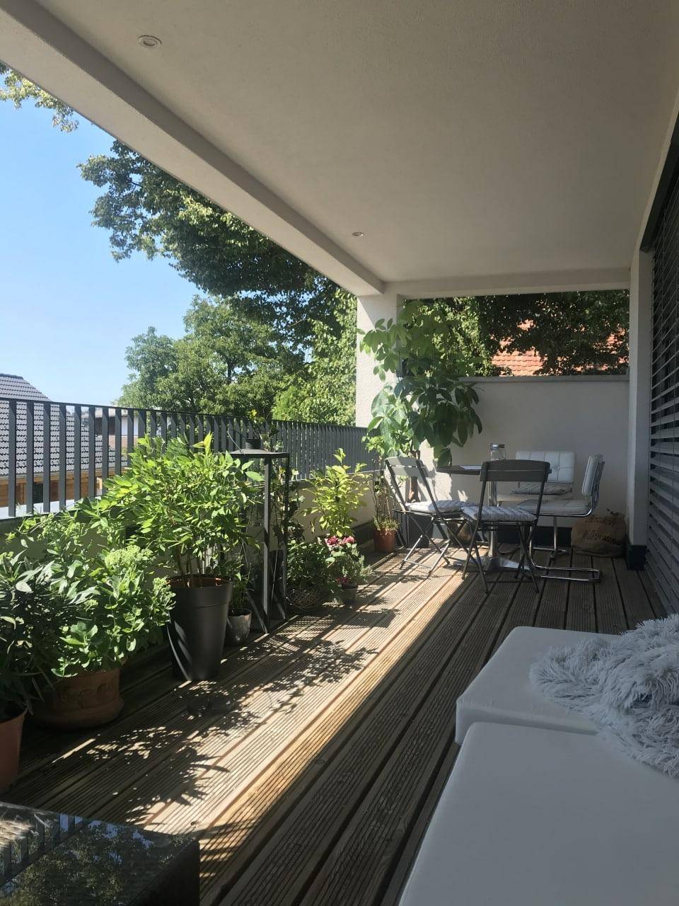 Sonniger Balkon mit Holzboden, vielen Pflanzen und Sitzgelegenheiten.