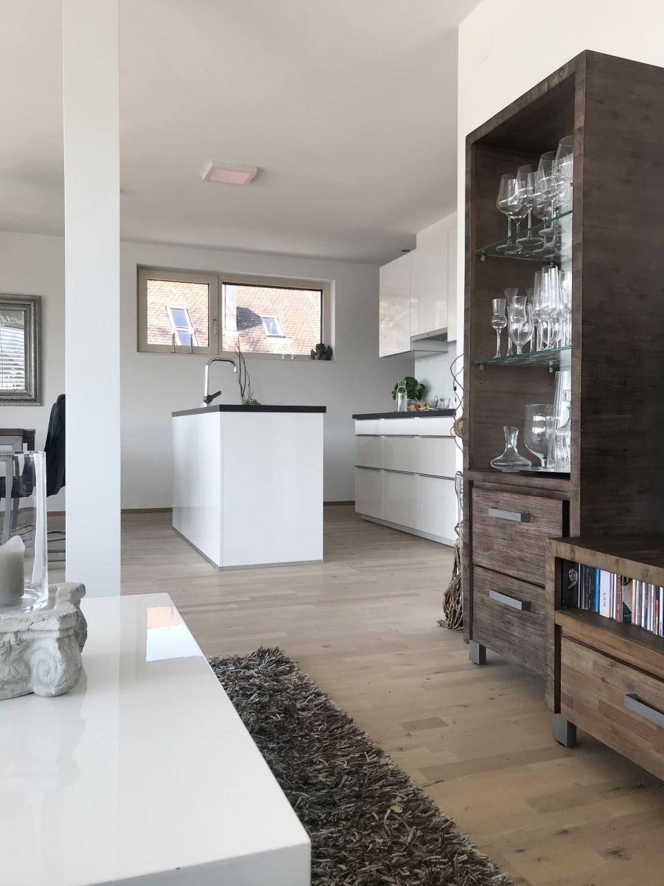 Moderne offene Küche mit weißer Insel und Holzboden, verbunden mit dem Wohnbereich.