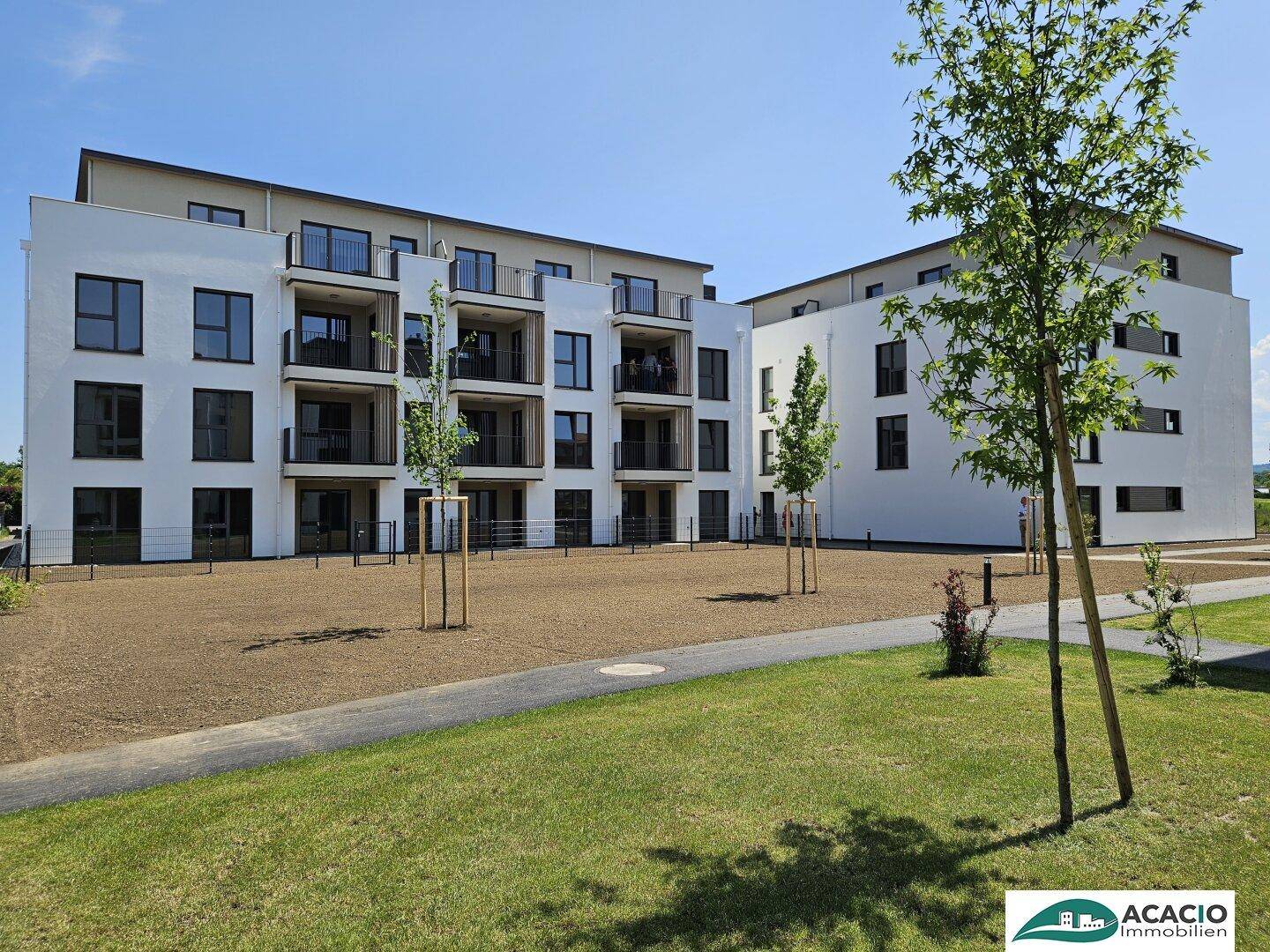 Moderne Wohngebäude mit weißer Fassade und Balkonen, umgeben von neu angelegten Grünflächen.
