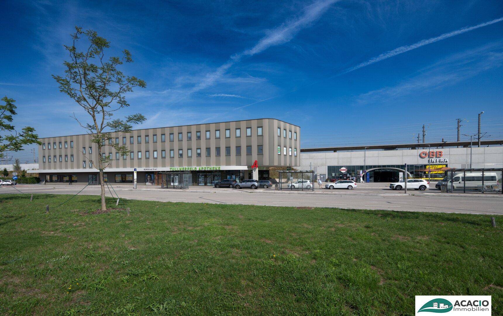 Außenansicht eines modernen Geschäftsgebäudes mit Parkplätzen und Grünflächen unter blauem Himmel.