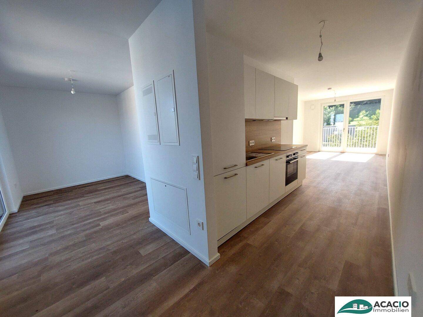 Heller, offener Wohnbereich mit neuer Einbauküche und Zugang zu einem Balkon.