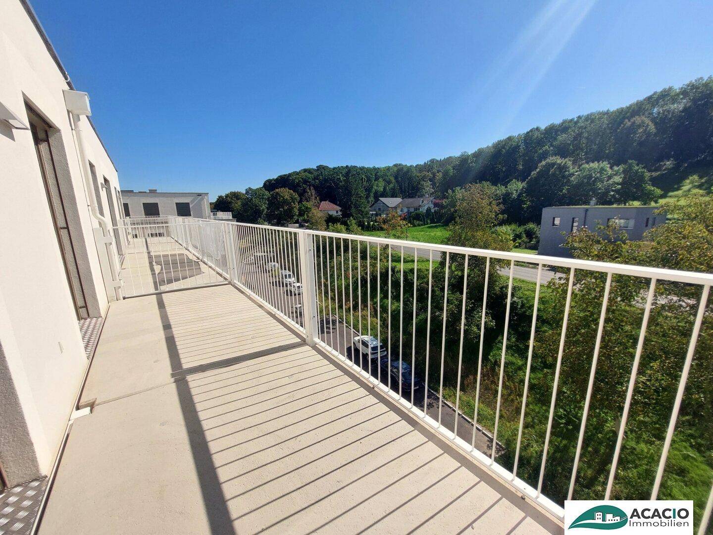 Langer Balkon mit weißem Geländer und weitem Blick ins Grüne und auf die Umgebung.
