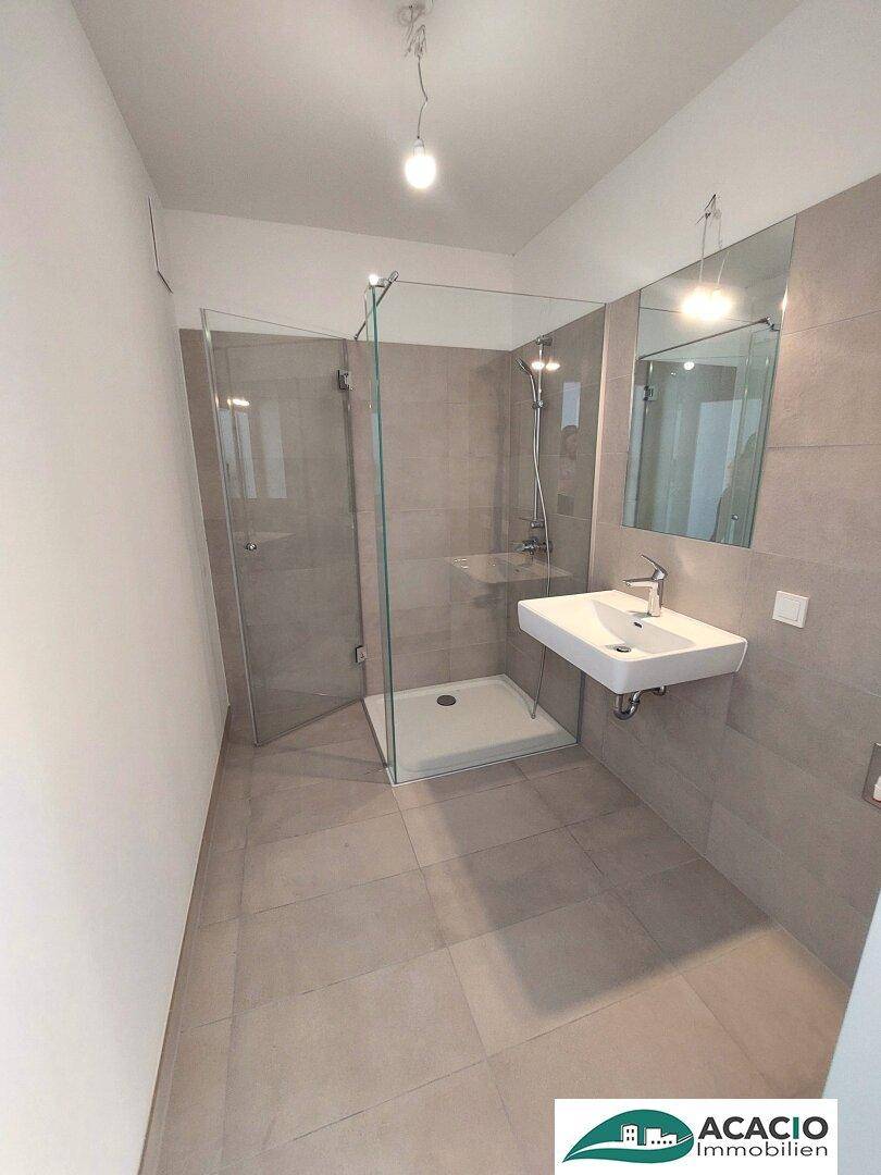 Modernes Badezimmer mit grauen Fliesen, ebenerdiger Dusche und wandhängendem Waschbecken.