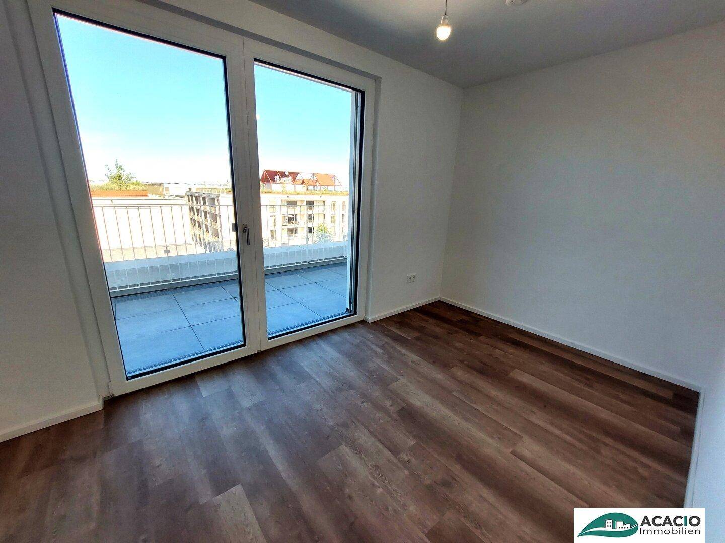 Helles Zimmer mit Laminatboden und Balkonzugang, bietet einen Blick auf die umliegenden Gebäude.