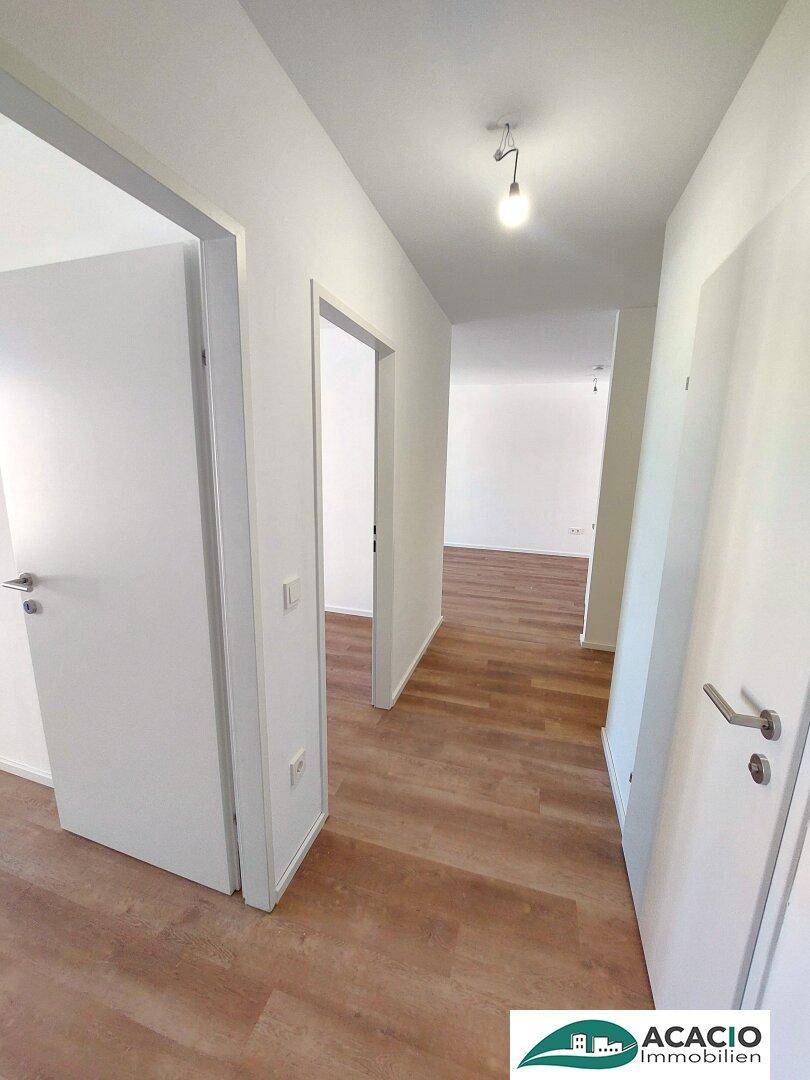 Heller Flur mit modernem Laminatboden und weißen Wänden, verbindet verschiedene Räume.