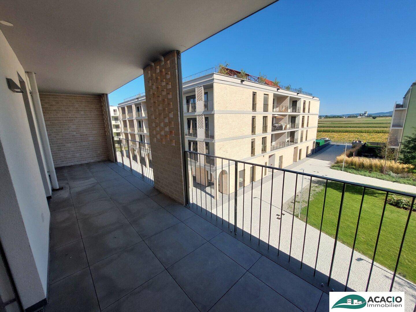 Geräumiger Balkon mit Fliesenboden und Blick auf umliegende Gebäude und Felder.