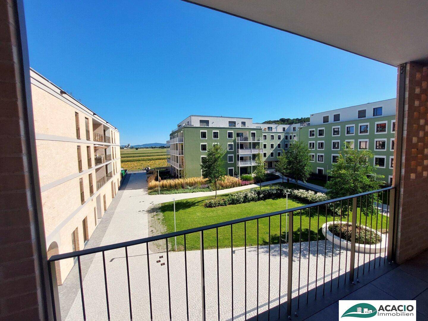 Balkon mit Blick auf einen gepflegten Gemeinschaftsgarten und moderne Wohngebäude.
