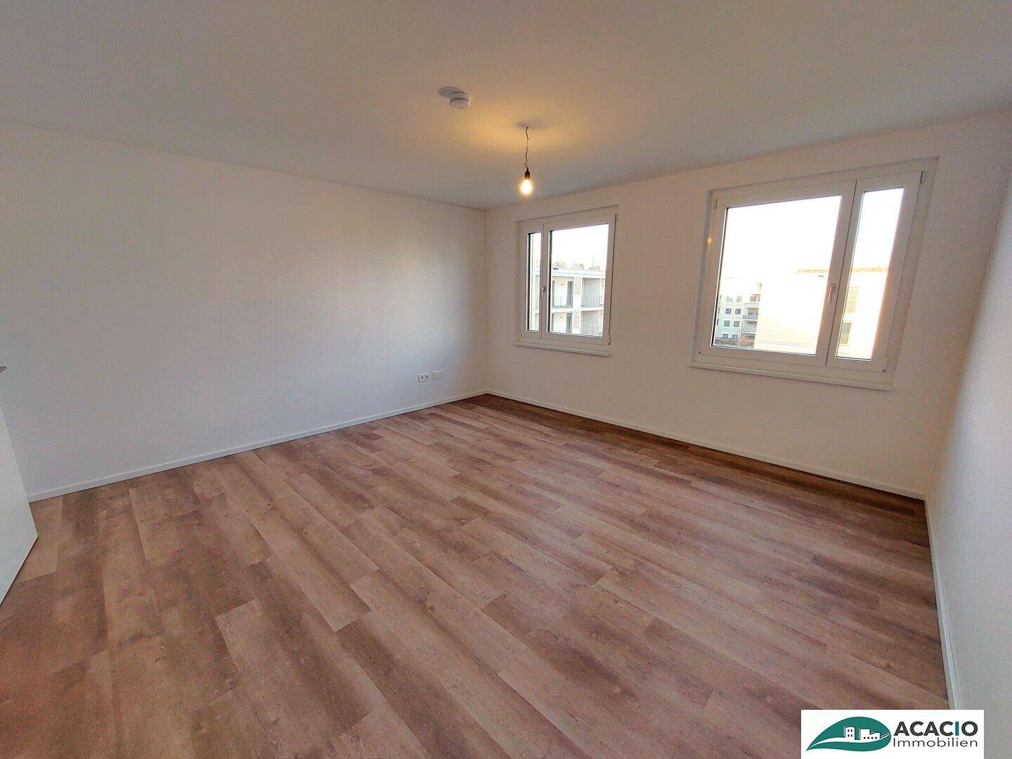 Helles Schlafzimmer mit zwei Fenstern, Laminatboden und viel Tageslicht.