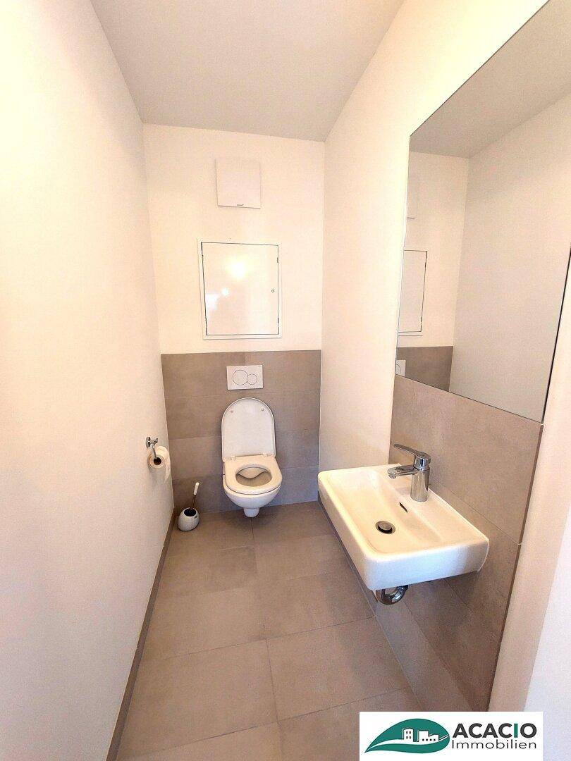 Gäste-WC mit wandhängendem WC, kleinem Waschbecken und modernen Fliesen.