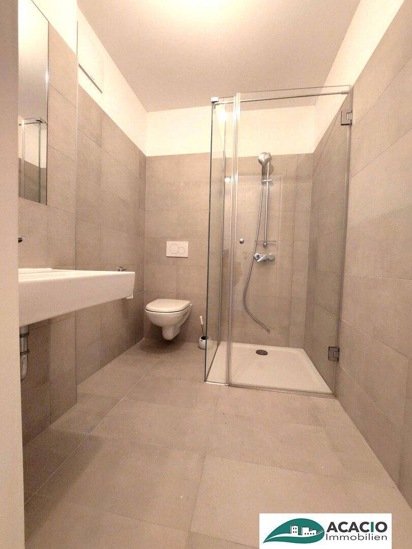Helles Badezimmer mit ebenerdiger Dusche, wandhängendem WC und modernen grauen Fliesen.