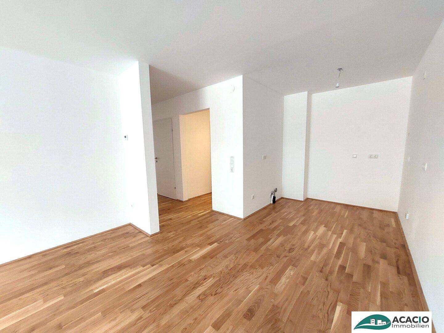 Geräumiger, leerer Wohnbereich mit hellem Parkettboden und Zugang zu weiteren Räumen.