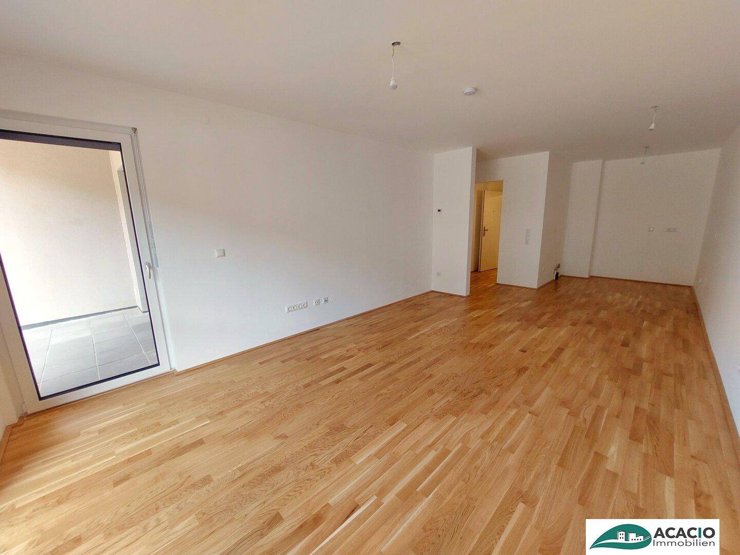 Lichtdurchfluteter Wohnraum mit Holzboden und einer großen Glastür, die nach draußen führt.