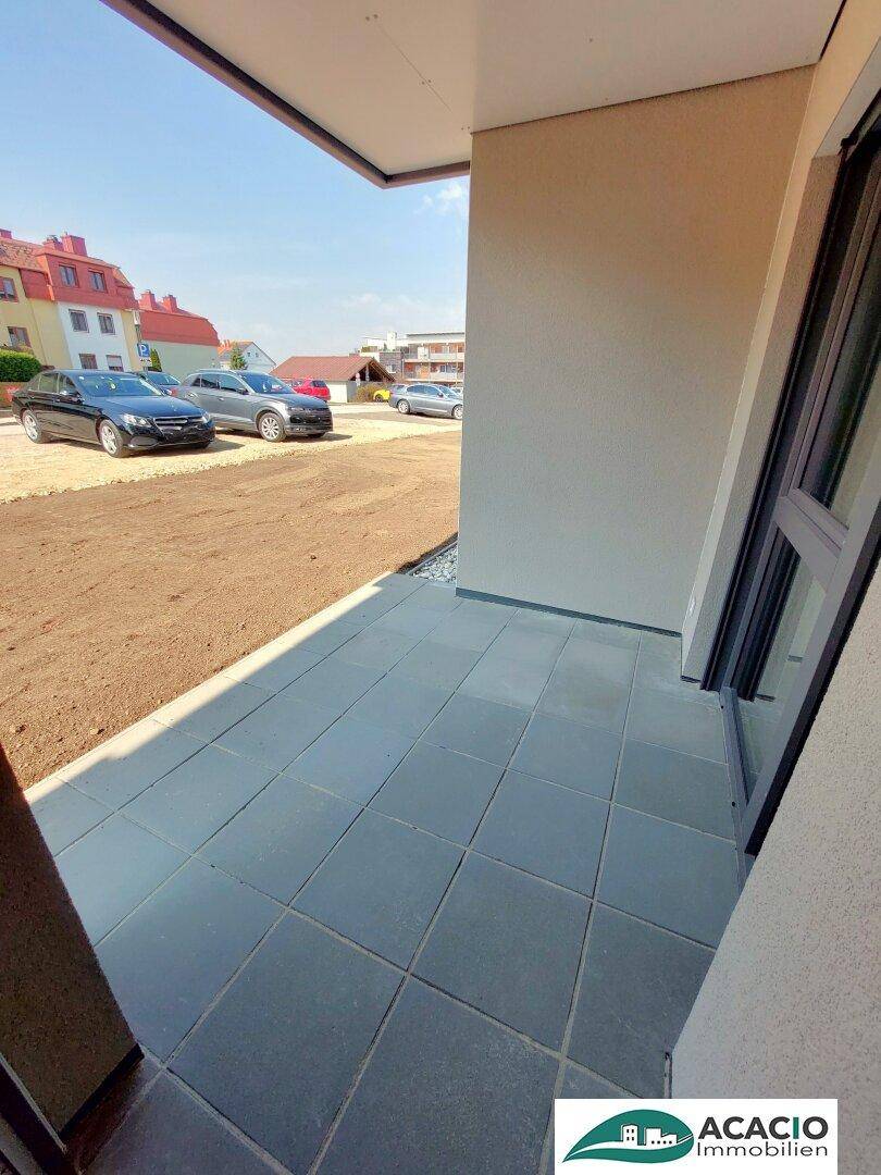 Geflieste Außenterrasse im Erdgeschoss mit Blick auf die Umgebung und Parkplätze.