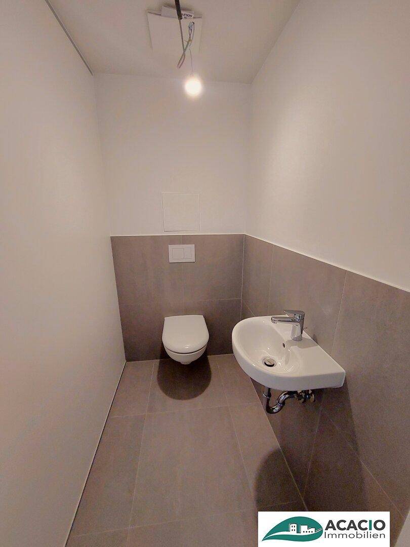 Gäste-WC mit wandhängender Toilette, kleinem Waschbecken und modernen Fliesen.