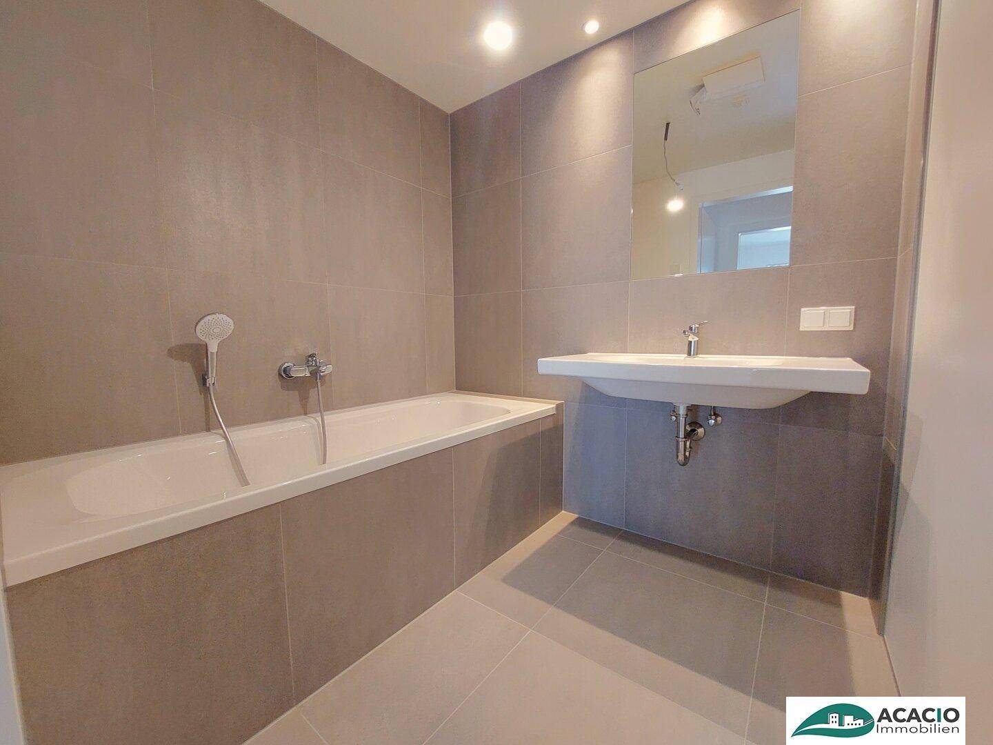 Modernes Badezimmer mit Badewanne, Einzelwaschbecken und grauen Fliesen.