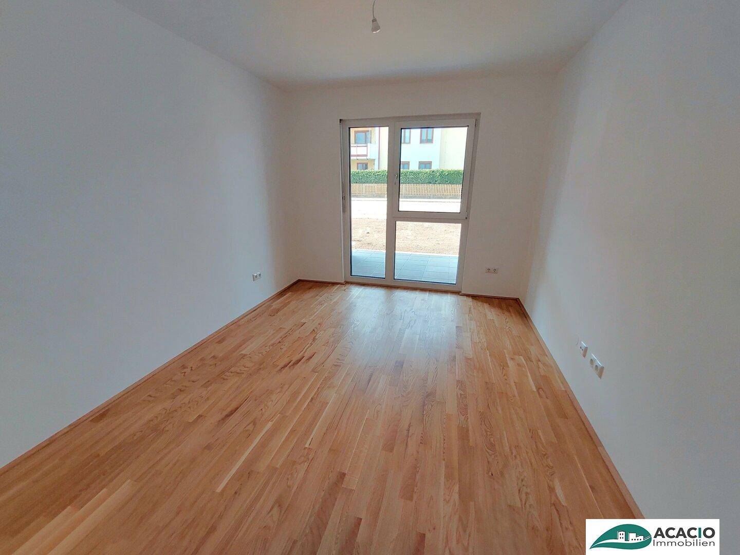 Leeres Schlafzimmer mit Parkettboden und direktem Zugang zu einem Außenbereich.