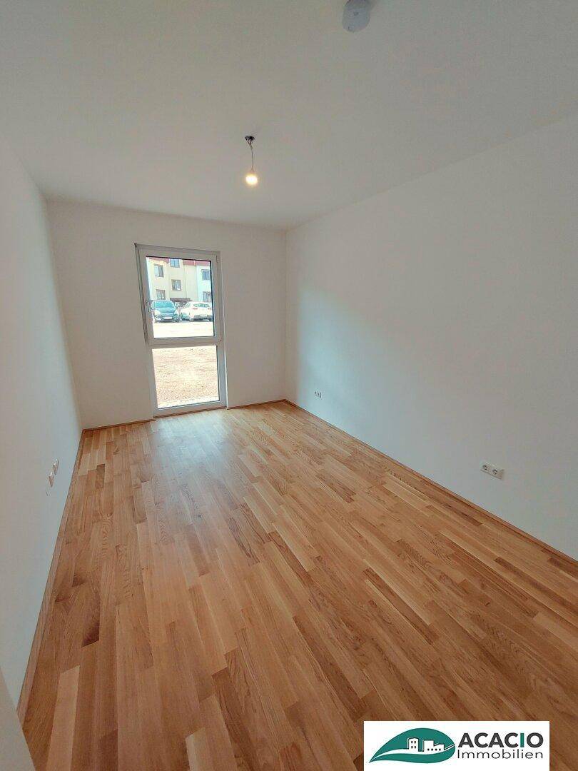 Lichtdurchflutetes Zimmer mit Parkettboden und Blick auf die Umgebung durch das Fenster.