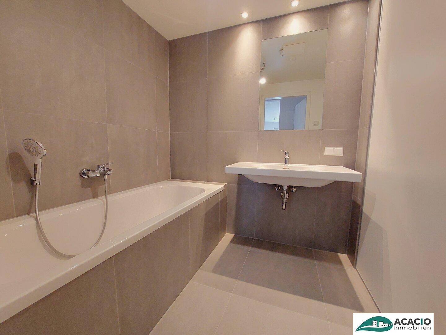 Modernes Badezimmer mit Badewanne, Waschtisch und grauen Fliesen in zeitgemäßem Design.
