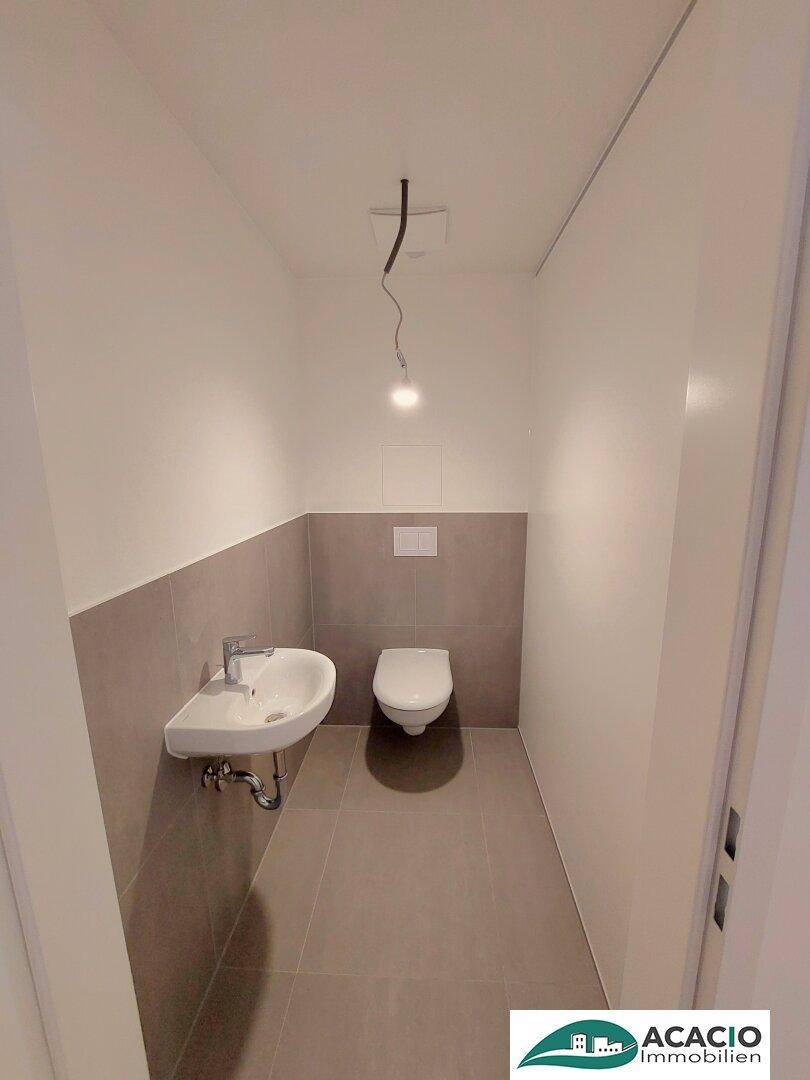 Modernes Gäste-WC mit Wand-WC, Waschbecken und grauen Fliesen an Wänden und Boden.