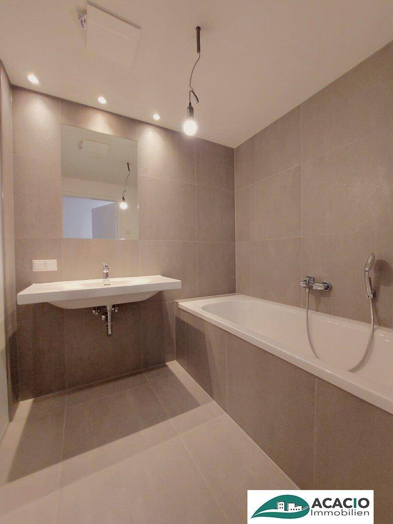 Modernes Badezimmer mit Badewanne, schwebendem Waschbecken und grauen Fliesen.