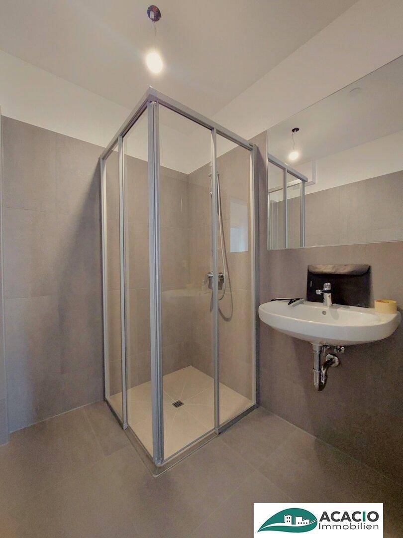 Modernes Badezimmer mit Duschkabine, Waschbecken und grauen Wand- und Bodenfliesen.